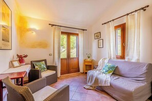 Ein gemütliches Wohnzimmer mit einer Couch, zwei Sesseln, einem kleinen Tisch und einer Tür, die in einen Garten führt.