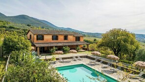Ein zweistöckiges Haus mit Swimmingpool, umgeben von üppiger Vegetation und Bergen.