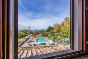 Une piscine avec une terrasse en pierre et des chaises longues, entourée de verdure et d’arbres.