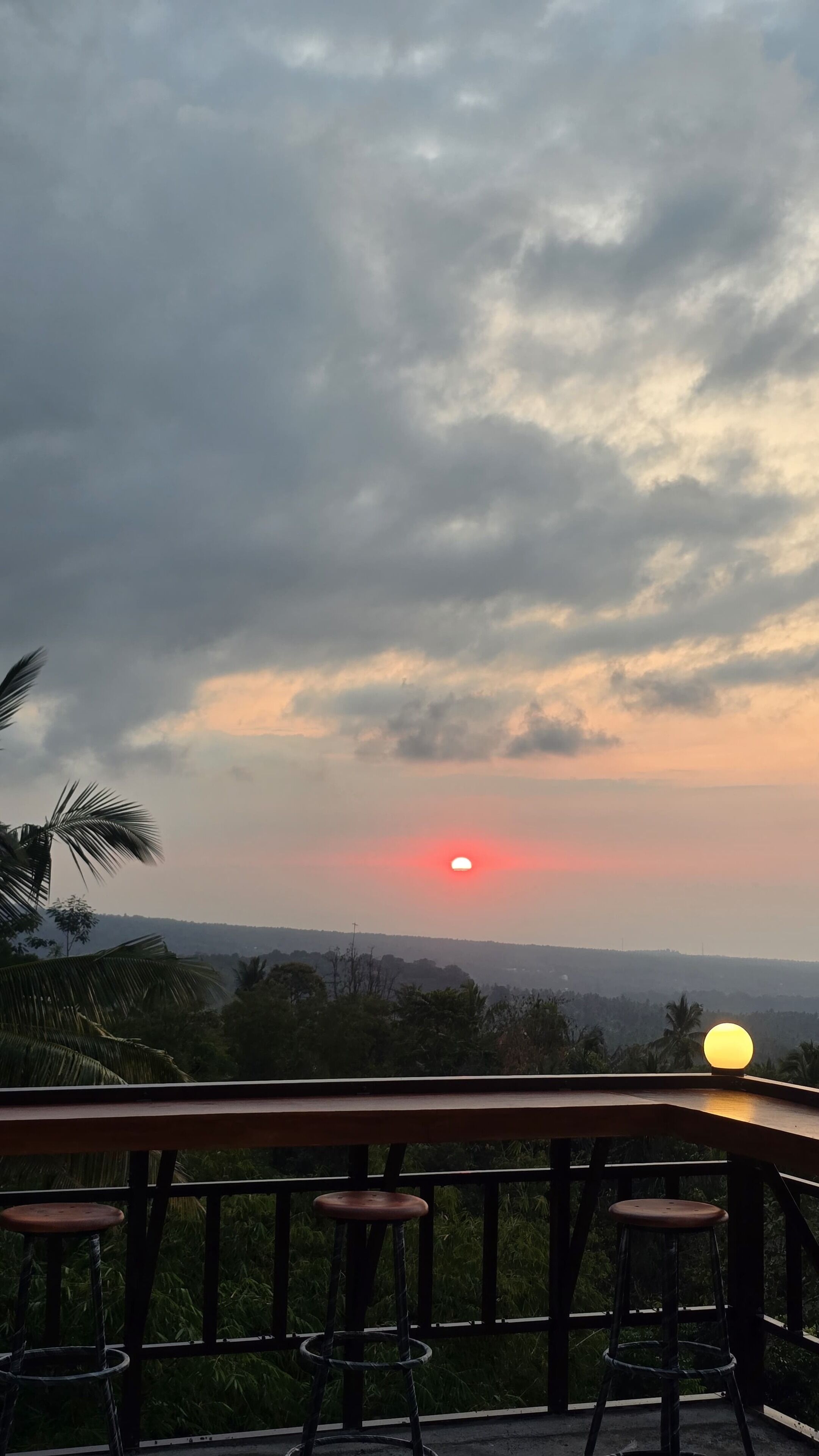 A sunset view from a balcony with a railing and two stools.