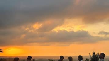 A group of people seated on outdoor chairs with a view of the sunset over a landscape.