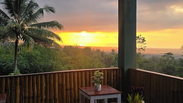 Un área de estar al aire libre con mesas y sillas, con vistas a un paisaje con palmeras y un atardecer.