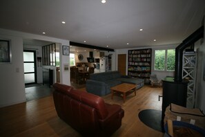 A spacious living area with a sofa, a coffee table, and a fireplace. There is a kitchen in the background and a bookshelf filled with books. - 100-square-meter apartment in a quiet location right in the heart of town (Saint-Pée-sur-Nivelle)