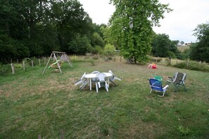 Un espacio al aire libre con un columpio, una mesa con sillas y una silla plegable azul.