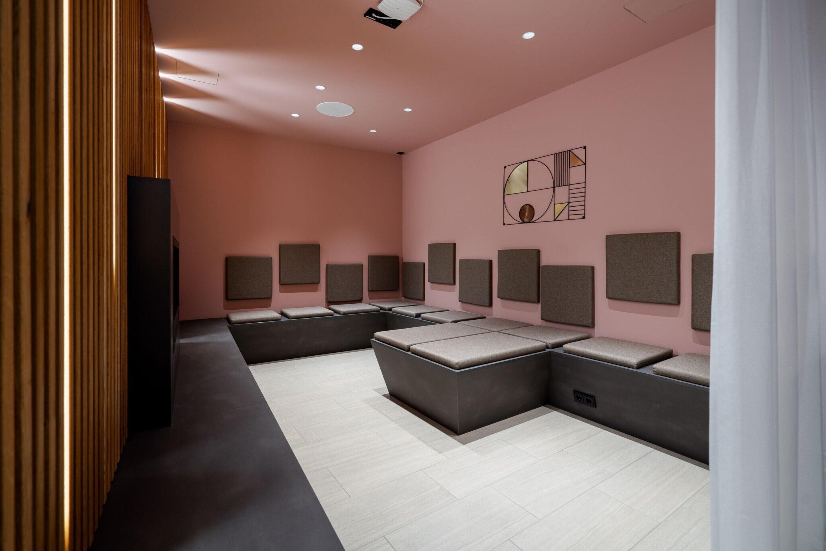 Una habitación moderna con una pared rosa, un amplio sofá modular y varios paneles insonorizados.