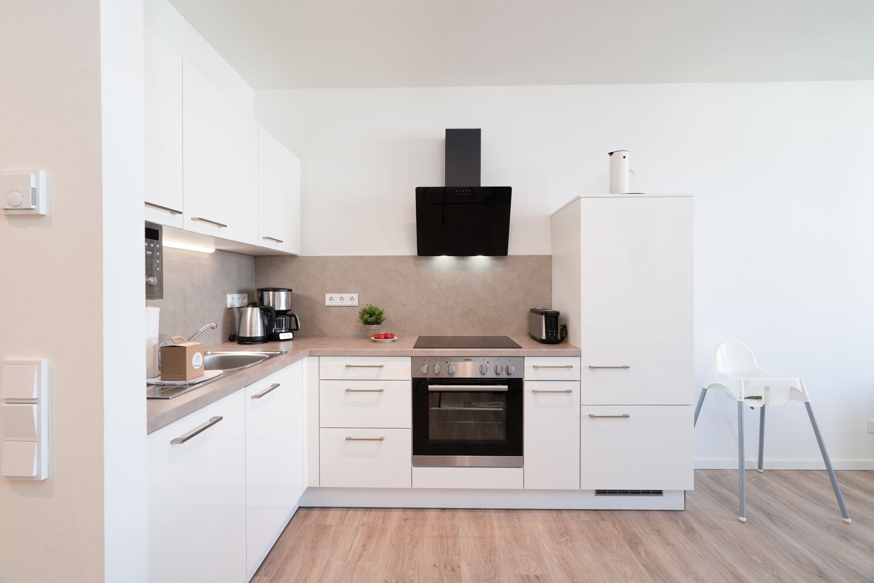 Une cuisine moderne avec des meubles blancs, une hotte noire et un four en acier inoxydable.