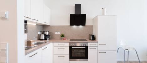 Une cuisine moderne avec des meubles blancs, une hotte noire et un four en acier inoxydable.