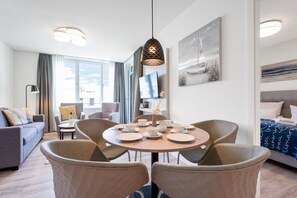 A modern hotel room with a dining area, a sofa, a TV, and a bed with a blue patterned bedspread. - Elegant Apartment With Sunny Loggia (Lübeck)