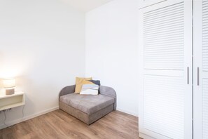 Ein kleiner, ordentlich eingerichteter Raum mit einer Couch, einer Lampe und einem Kleiderschrank.