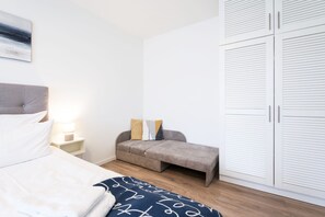 Quarto com cama, mesa de cabeceira com luminária, sofá e guarda-roupa.