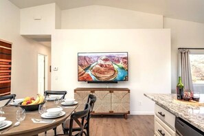 A modern kitchen with a dining area, a flat-screen TV mounted on the wall, and a buffet-style table with fruit and glasses. - 35-45 Grasshopper Lane combo ·Large retreat, red rock views, spas, six king beds (Sedona)
