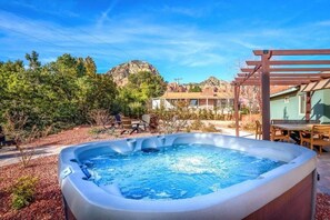 Ein Whirlpool in einem Garten mit einer Pergola, einem Tisch und Stühlen.