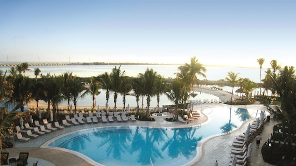 Ein Hotelpool mit Liegestühlen und Palmen, mit Blick auf einen Strand und das Wasser.