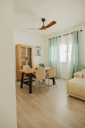 Um quarto com uma mesa de jantar de madeira, cadeiras, um armário com portas de vidro, um ventilador de teto e um sofá.