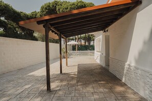 A covered outdoor area with a pergola structure, a white wall, and a paved floor. - Villa Los Gallos (Chiclana de la Frontera)
