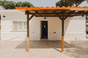 Un edificio con un vestíbulo cubierto, una puerta y un ventanal con rejas.