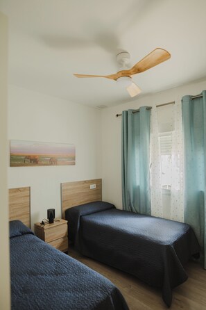 A bedroom with two beds, a ceiling fan, a nightstand, a painting, and curtains. - Villa Los Gallos (Chiclana de la Frontera)
