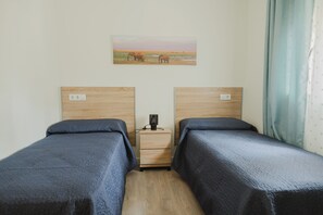 Quarto de hotel com duas camas de solteiro, mesa de cabeceira com abajur e um quadro de elefantes na parede.