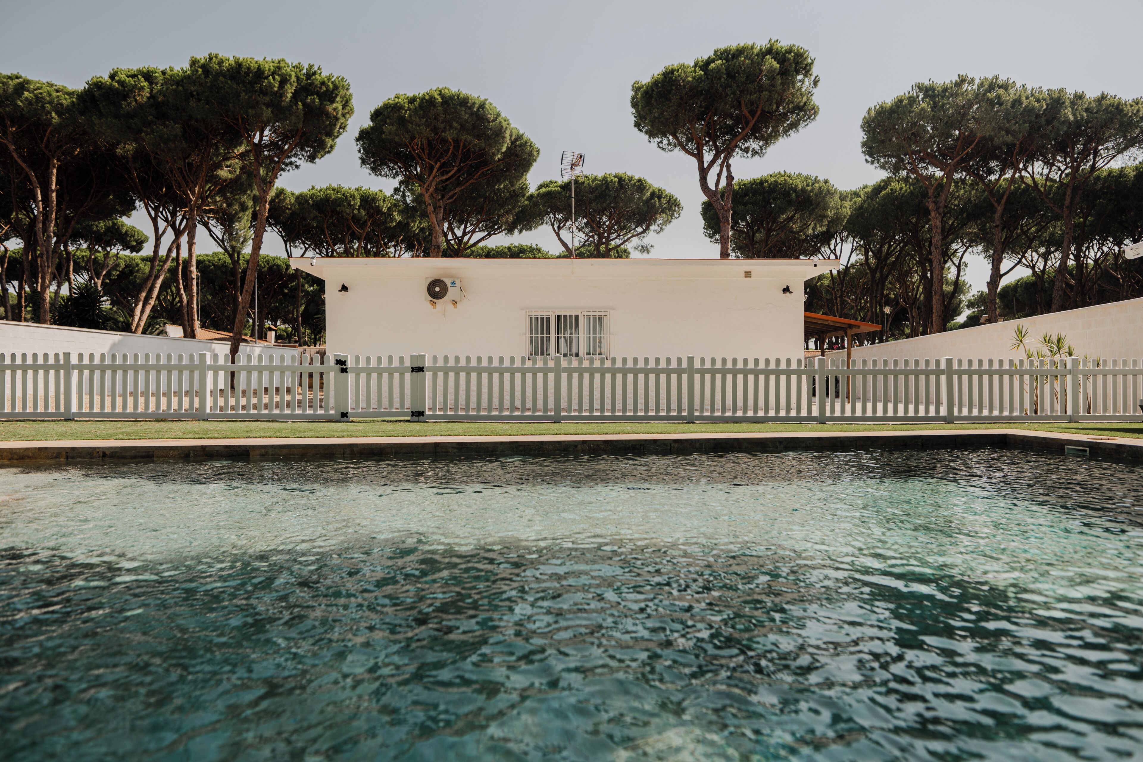 A swimming pool with a white fence and trees in the background.