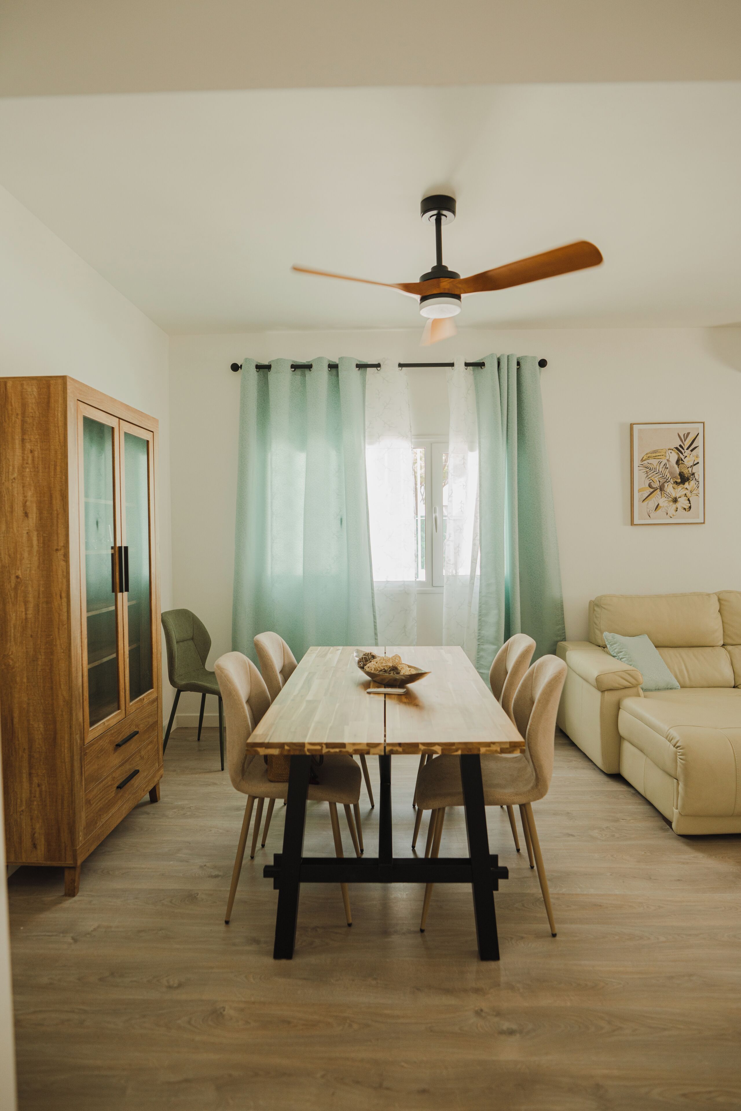 Un comedor con una mesa, sillas, un armario de madera y un ventilador de techo.