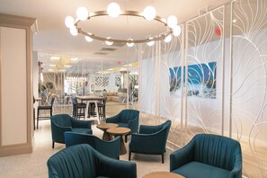 Un espace détente moderne avec des fauteuils turquoise, des tables rondes et un panneau décoratif blanc.