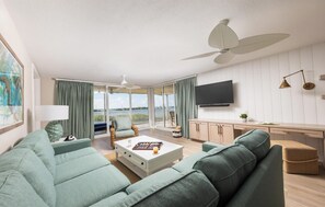 A spacious living room with a large sofa, a coffee table, and a television. There is a balcony with a view of the sea. - Bright Location — Outdoor Pool Access, Full Kitchen and Near Beach (Duck Key)