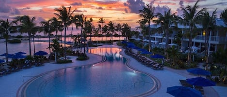 Ein Poolbereich eines Resorts mit Palmen, Liegestühlen und Sonnenschirmen.