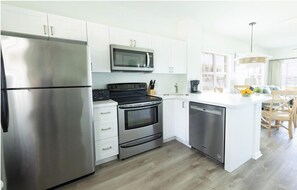 A modern kitchen with stainless steel appliances, white cabinetry, and a wooden dining area. - Amazing Location in the Middle of Florida Keys! Full Kitchen! Onsite Pools (Duck Key)