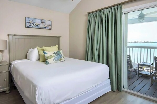 Ein Hotelzimmer mit einem großen Bett, einem Nachttisch, einem Fenster mit Vorhängen und Blick aufs Meer.