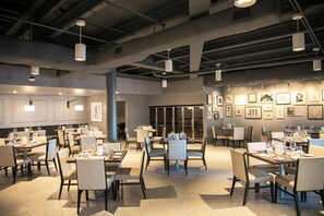 A spacious restaurant with multiple dining tables and chairs, overhead lighting, and framed artwork on the walls. - Island-Style Living with a Full Kitchen and Direct Access to Pool Near Key Largo (Duck Key)
