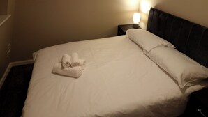 A neatly made bed with white linens and a set of towels on the side.