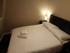 A neatly made bed with white linens and a set of towels on the side.