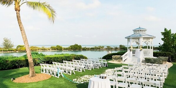 A wedding ceremony setup with white chairs arranged in rows, a white gazebo, and a palm tree. - Unwind with Pool Access and Kitchen Near Lagoon | Duck Key Escape (Duck Key)