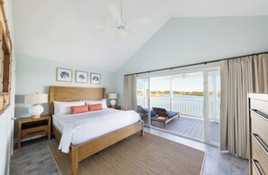 Ein Schlafzimmer mit Bett, Nachttischen, Deckenventilator und Balkon mit Stuhl.