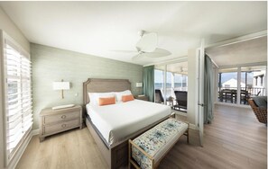 Ein Hotelzimmer mit Bett, Nachttisch, Lampe und Blick auf Balkon und die Außenwelt.