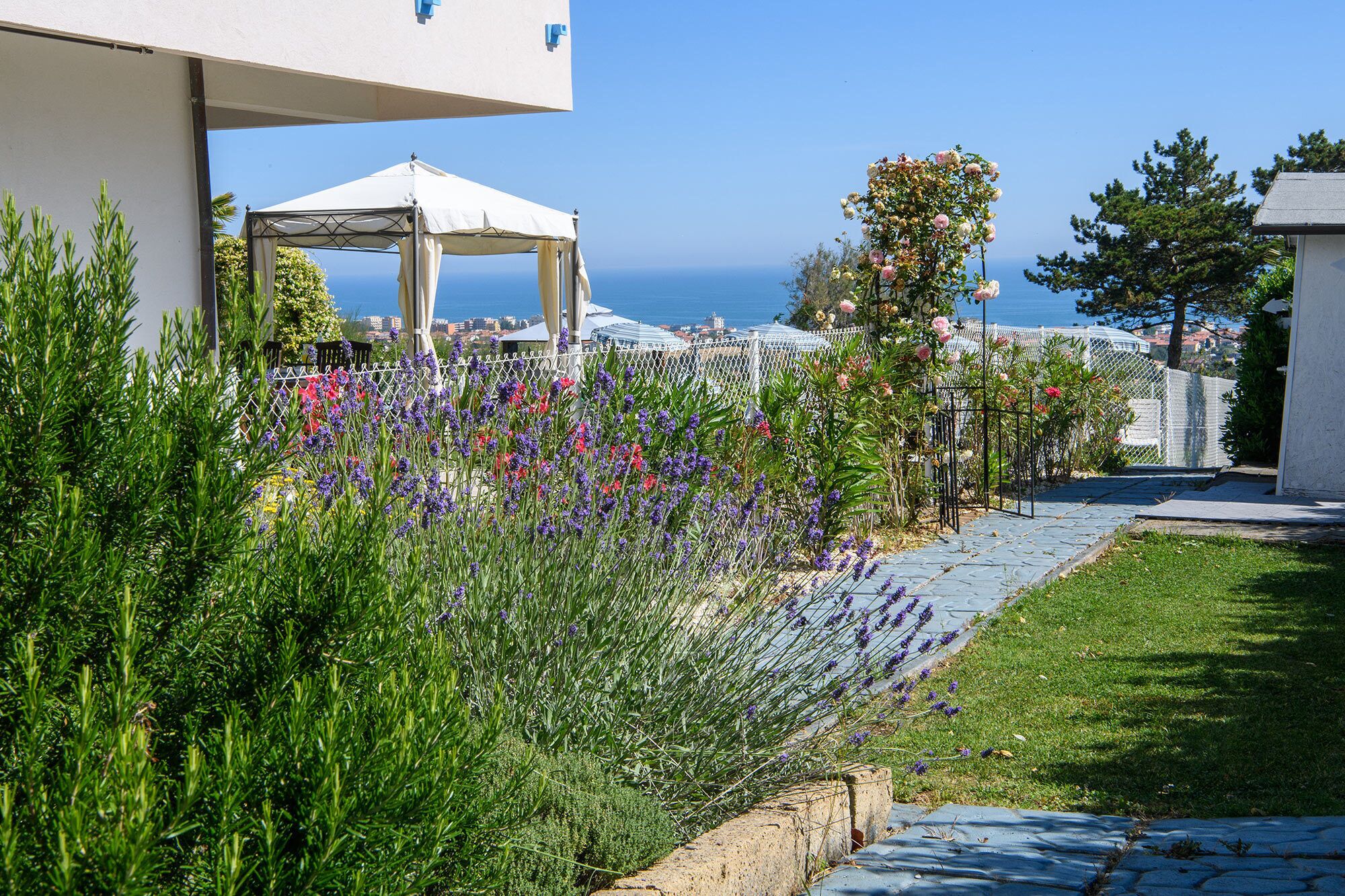 Un giardino con un vialetto che conduce a un edificio bianco dotato di area salotto esterna coperta.