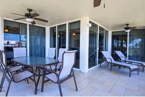 Eine Terrasse im Freien mit einem runden Tisch und Stühlen, Deckenventilatoren und Glastüren, die zu einem Poolbereich führen.