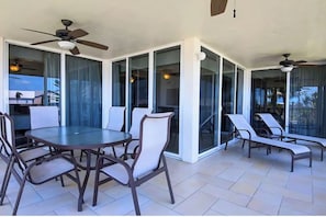 Eine Terrasse im Freien mit einem runden Tisch und Stühlen, Deckenventilatoren und Glastüren, die zu einem Poolbereich führen.