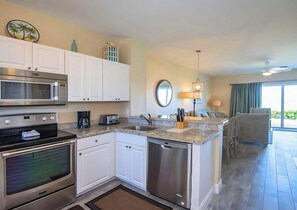A modern kitchen with white cabinets, stainless steel appliances, a granite countertop, and a view to the living area. - Beautiful Pool Access and In-Room Kitchen Make this the Perfect Island Getaway! (Duck Key)