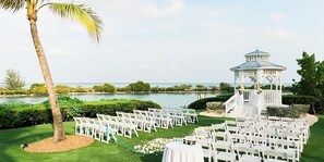 Une cérémonie de mariage avec des chaises blanches disposées en rangées, un gazebo blanc et un palmier.