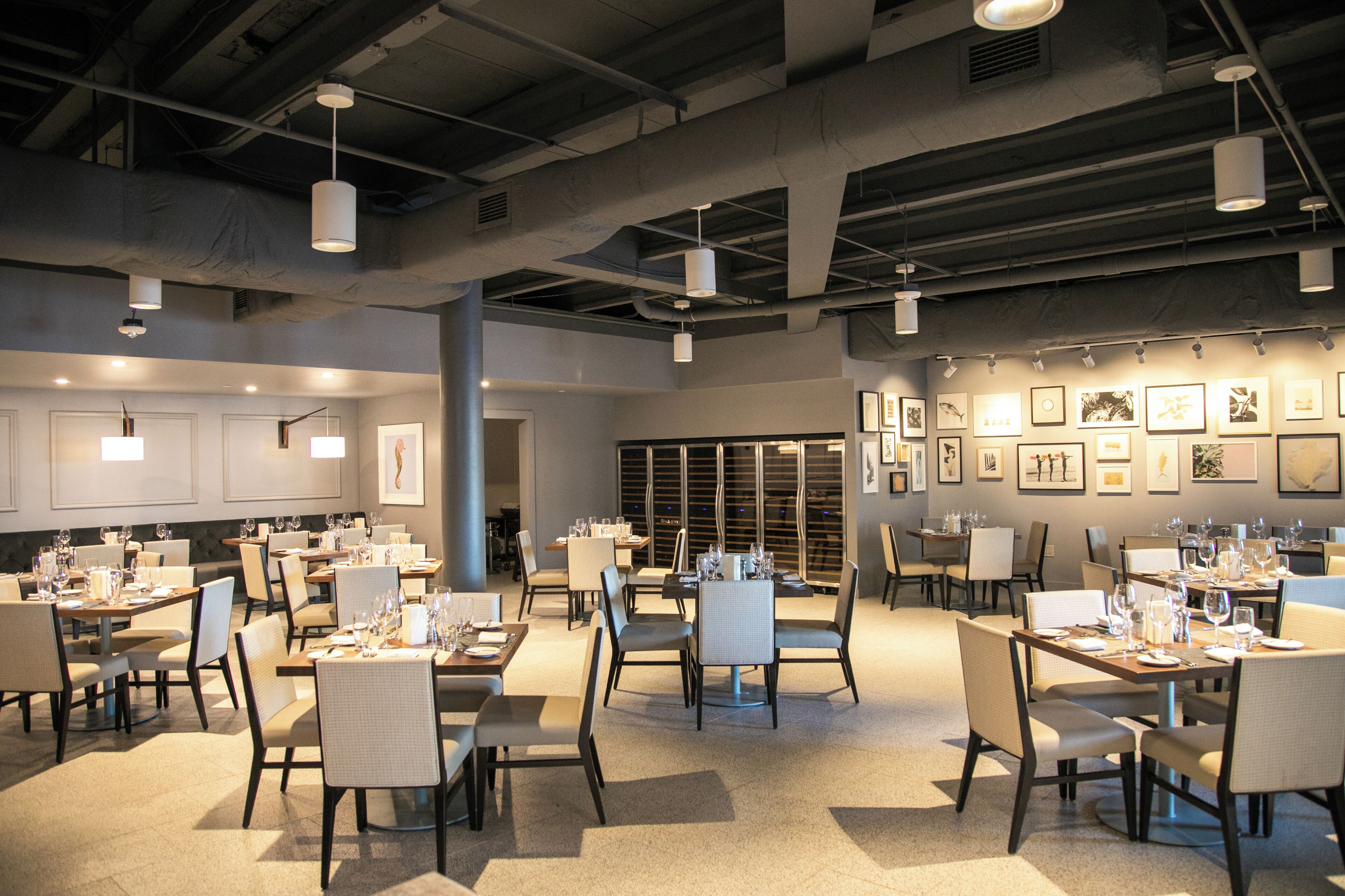 Ein geräumiges Restaurant mit mehreren Esstischen und Stühlen, Deckenleuchten und gerahmten Bildern an den Wänden.