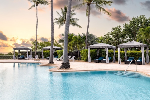 A pool area with lounge chairs and umbrellas, surrounded by palm trees and a sunset view. - Charming Villa with Pool Access & Full Kitchen for Easy Meals! (Duck Key)