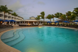 A swimming pool with lounge chairs and umbrellas, surrounded by palm trees and a hotel building. - A Perfect Mix of Comfort and Convenience with Pool Access and Full Kitchen! (Duck Key)