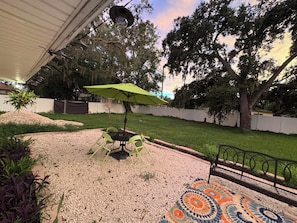 A patio with a table and chairs, surrounded by a gravel area with a decorative rug.