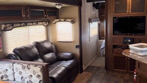 Interior compacto de una autocaravana con zona de estar, kitchenette y televisor.