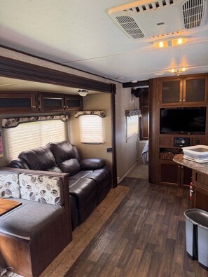Un intérieur de camping-car compact comprenant un coin salon, un coin cuisine et un téléviseur.