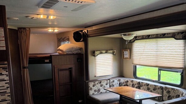 Interior de una caravana compacta con kitchenette, zona de comedor y ventana con vistas al exterior.