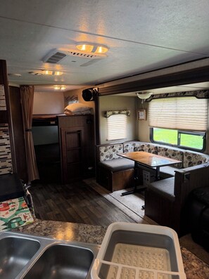 A compact RV interior with a kitchenette, a dining area, and a window providing a view of the outdoors.