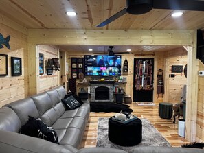 A cozy living room with a leather sofa, a fireplace, and a flat-screen TV mounted on the wall. - Wolf Creek Cabin Waterfront/Secluded/Firepit/VA Creeper Trail/South Holston Lake (Abingdon)
