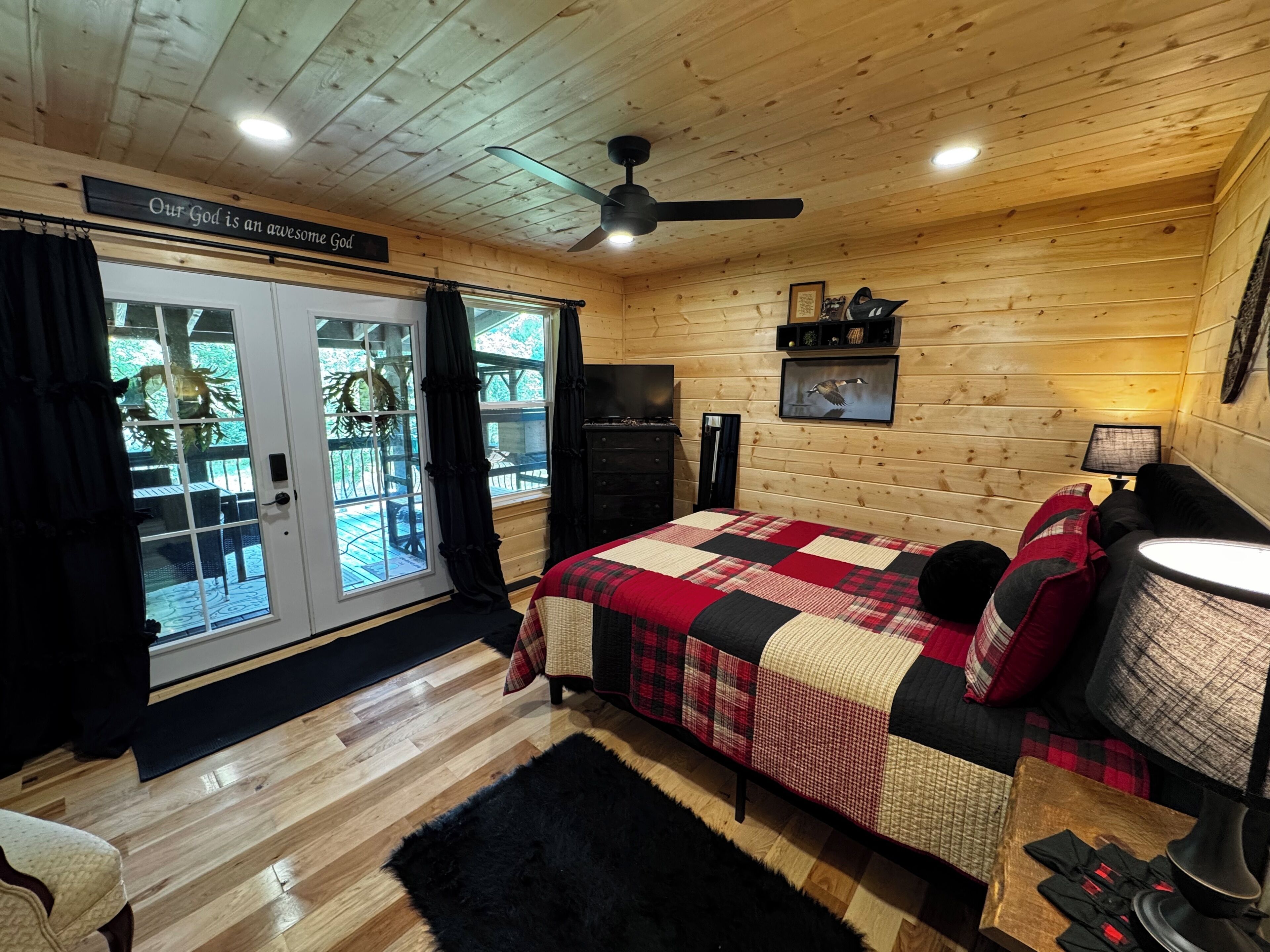 A cozy cabin room with a bed, a desk, a chair, and a window overlooking a deck.